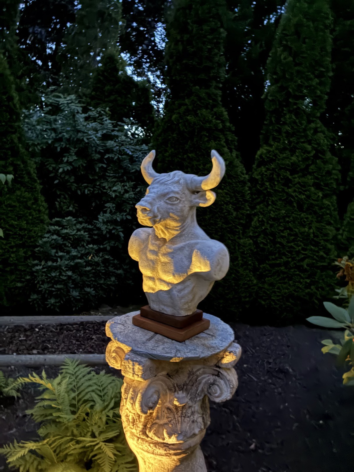 The minotaur sculpture uplit against dark evergreens at nightfall.